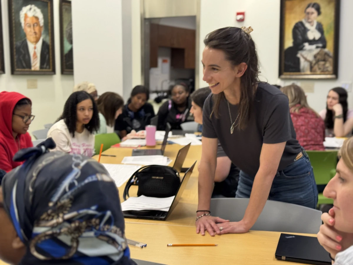 Stephanie teaching at a workshop table, leaning in over the students' work